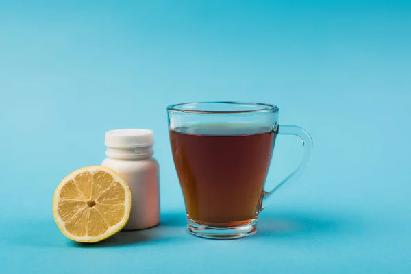 Чашка чая рядом с лимоном и таблетки на голубом фоне — стоковое фото