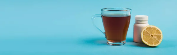 Cup of tea near jar with pills and lemon on blue background, banner - foto de stock