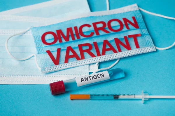 Test tube with antigen lettering near medical masks and syringe on blue background - foto de stock