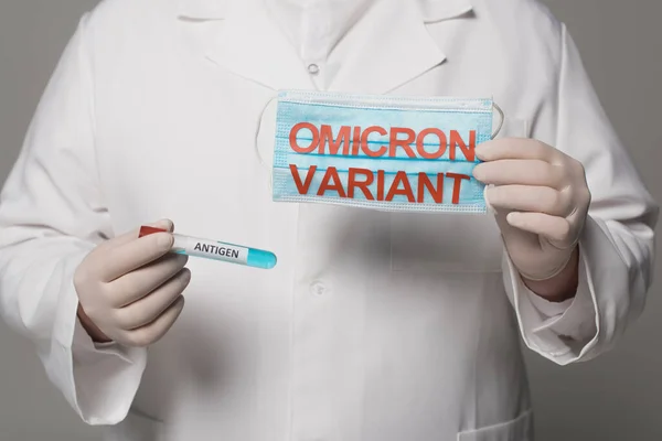 Cropped view of doctor holding medical mask with omicron variant and test tube with antigen lettering isolated on grey - foto de stock