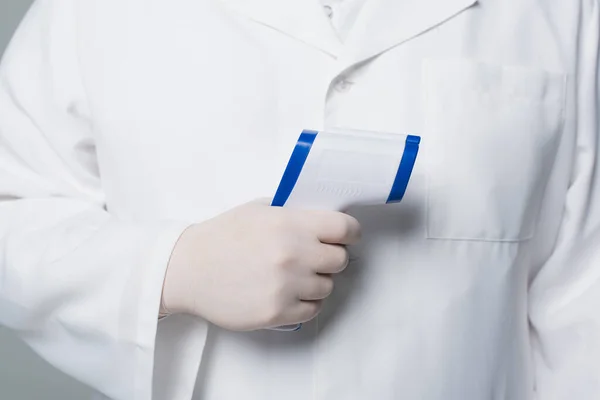 Cropped view of doctor in white coat and latex glove holding pyrometer isolated on grey — Photo de stock