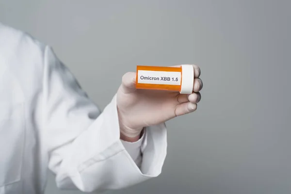 Cropped view of doctor in latex glove holding pills with omicron xbb lettering isolated on grey - foto de stock