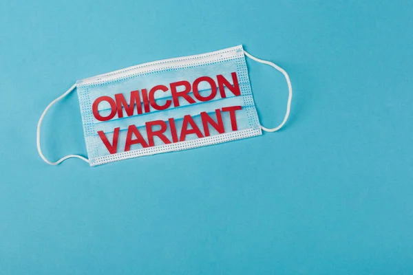 Top view of medical mask with omicron variant lettering on blue background with copy space - foto de stock