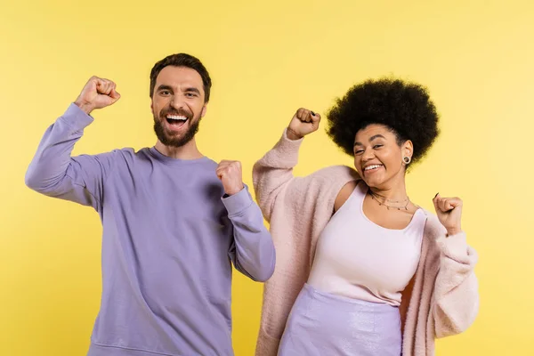 Excited interracial couple looking at camera and celebrating success isolated on yellow — Stock Photo