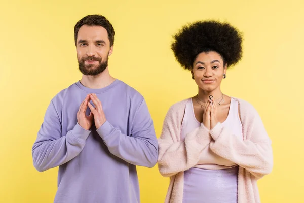 Cunning interracial couple smiling at camera and showing please gesture isolated on yellow — Stock Photo