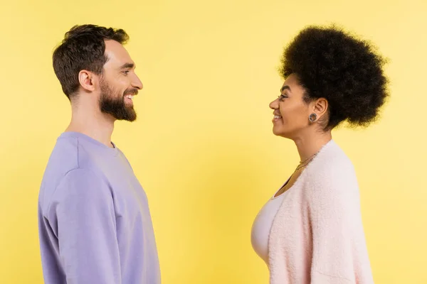 Side view of stylish african american woman and bearded man smiling at each other isolated on yellow — Stockfoto
