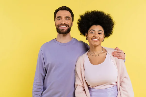 Happy bearded man hugging shoulders of stylish african american woman while looking at camera isolated on yellow — Stock Photo
