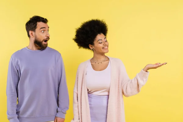 Smiling african american woman pointing with hand near amazed bearded man isolated on yellow — Photo de stock