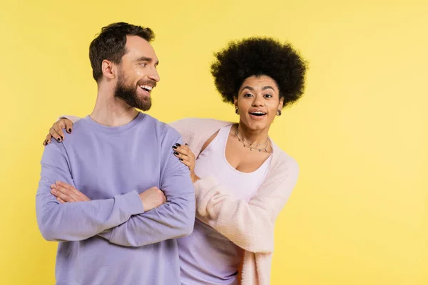 Happy and trendy african american woman hugging shoulders of cheerful bearded man isolated on yellow - foto de stock