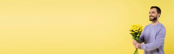 Cheerful bearded man holding bouquet and looking away isolated on yellow, banner - foto de stock