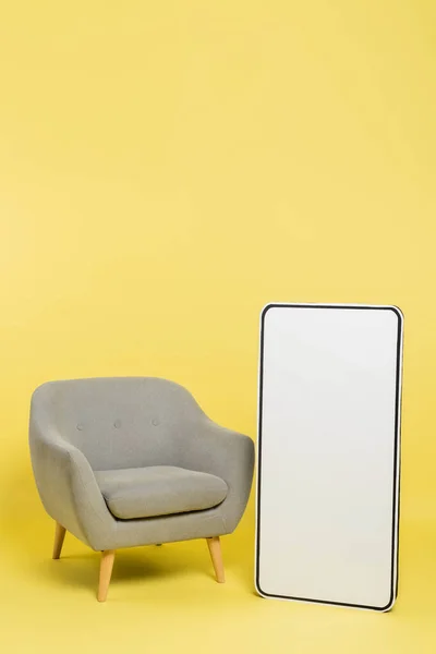 Vertical view of white mock-up of mobile phone near grey armchair on yellow background — Stock Photo