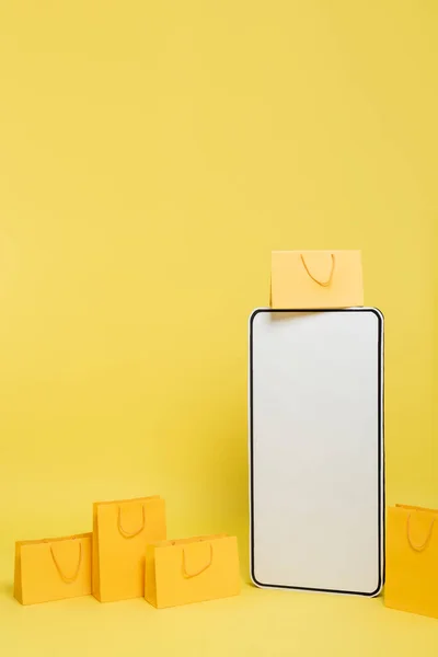 Vertical view of huge mock-up of smartphone near shopping bags on yellow background — Stockfoto