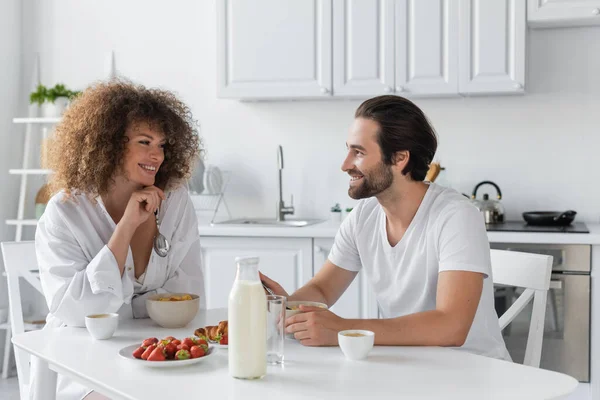 Cheerful young woman having breakfast with bearded boyfriend in kitchen — Fotografia de Stock