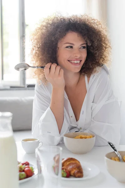Cheerful young woman holding spoon while having breakfast in kitchen — Photo de stock