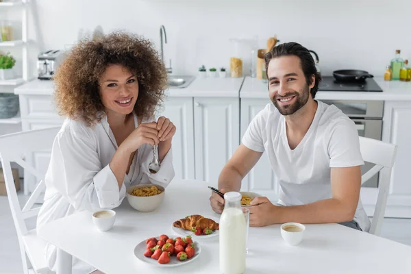 Cheerful young man having breakfast with curly girlfriend in kitchen — Stock Photo