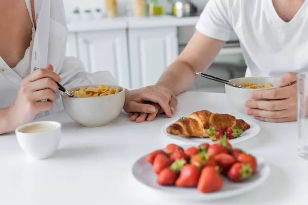 Cropped view of young couple holding hands near delicious breakfast on table — Stock Photo