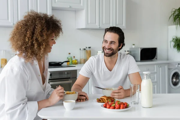 Happy bearded man smiling while looking at curly girlfriend during breakfast — Foto stock