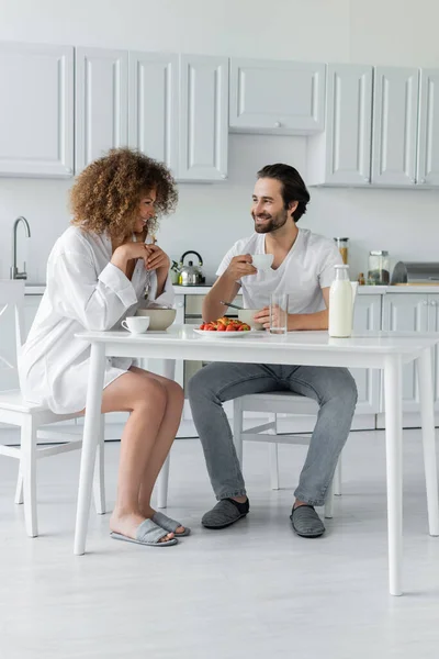 Full length of happy young man having breakfast with curly girlfriend in kitchen — Foto stock