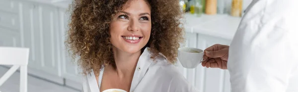 Man giving cup of coffee to cheerful girlfriend in kitchen, banner — Stock Photo