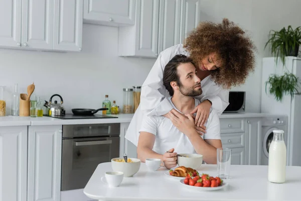 Curly young woman hugging bearded boyfriend during breakfast in kitchen — Foto stock