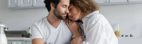 Curly woman leaning on shoulder of bearded boyfriend in kitchen, banner — Stock Photo
