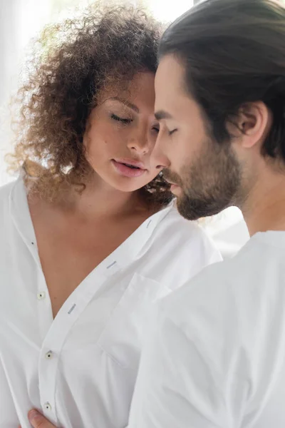Bearded man with closed eyes near sensual girlfriend in white shirt - foto de stock