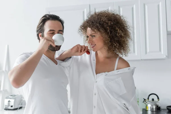 Curly woman holding red and fresh strawberry near bearded boyfriend drinking coffee — Stock Photo