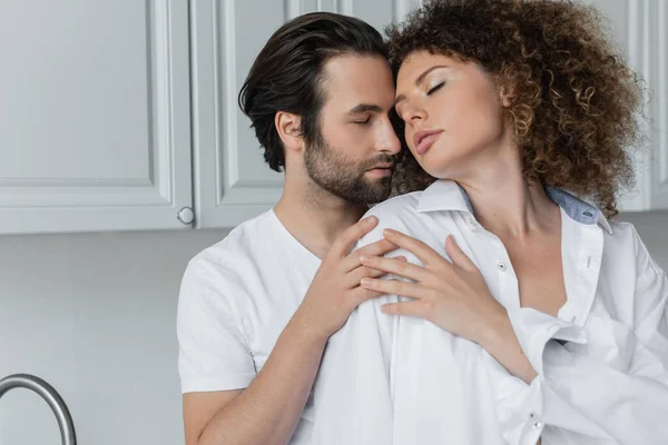 Bearded man seducing sexy and curly woman with closed eyes in kitchen - foto de stock