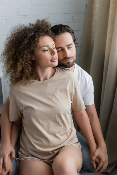 Young woman with closed eyes sitting with bearded boyfriend - foto de stock