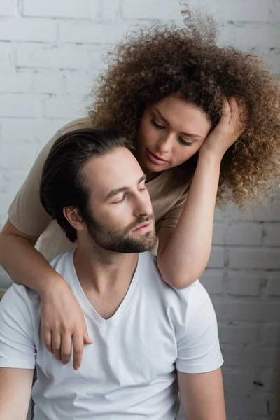 Curly young woman hugging and looking at bearded man in white t-shirt — Fotografia de Stock