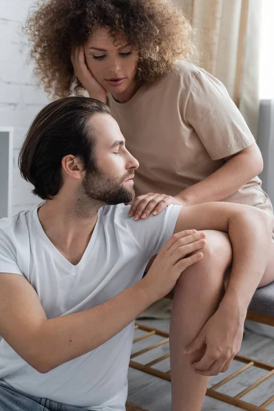 Curly woman sitting on bed bench near bearded man in white t-shirt — Stock Photo