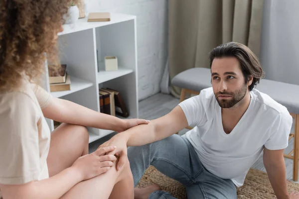 Curly woman sitting and touching hand of bearded boyfriend in bedroom — Stock Photo
