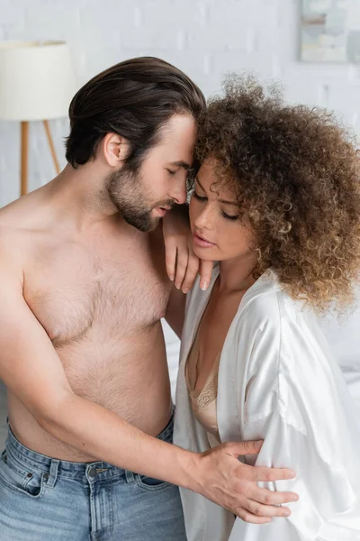 Shirtless man seducing curly young girlfriend in white satin robe - foto de stock