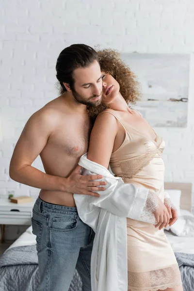Shirtless man in jeans standing with seductive woman in night dress and silk robe — Foto stock