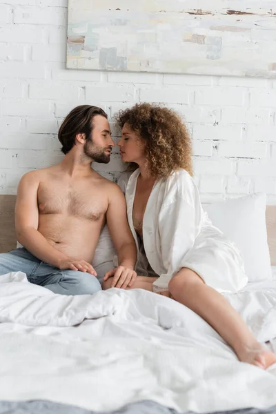 Side view of young and sexy couple with closed eyes sitting on bed — Stockfoto