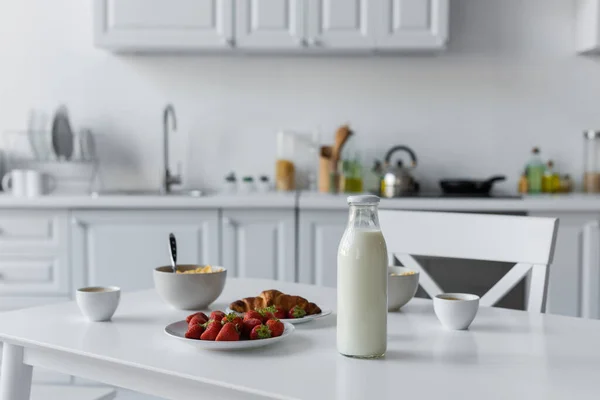 Glass bottle with milk near tasty breakfast on table in kitchen — Stock Photo