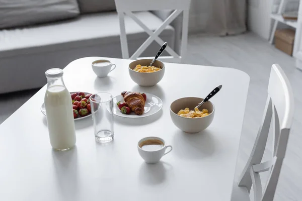 Vista de ángulo alto de botella de vidrio con leche cerca de tazas con café y sabroso desayuno en la mesa en la cocina - foto de stock