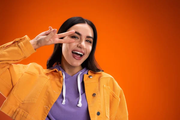 Cheerful young woman showing peace sign at camera isolated on orange — Foto stock