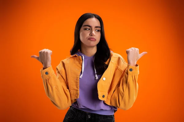 Skeptical brunette woman pointing with fingers isolated on orange — Stock Photo