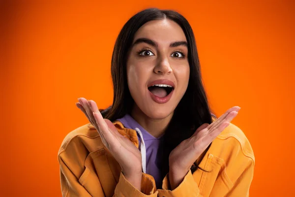 Portrait of excited brunette woman looking at camera isolated on orange — Stockfoto