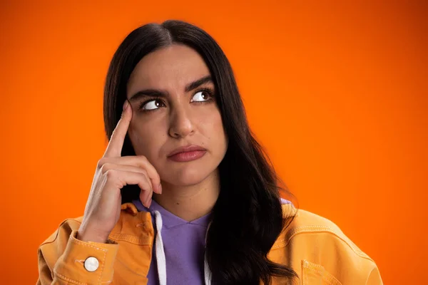 Portrait of pensive woman holding finger near eyebrow isolated on orange — Foto stock
