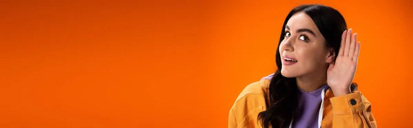 Smiling brunette woman listening isolated on orange, banner — Foto stock