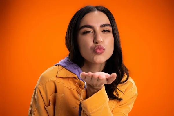 Portrait of brunette woman blowing kiss at camera isolated on orange — Stockfoto