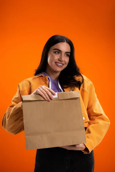 Smiling woman in casual clothes holding paper bag isolated on orange — Foto stock
