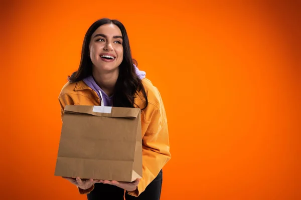 Cheerful woman holding paper bag with food isolated on orange — Fotografia de Stock