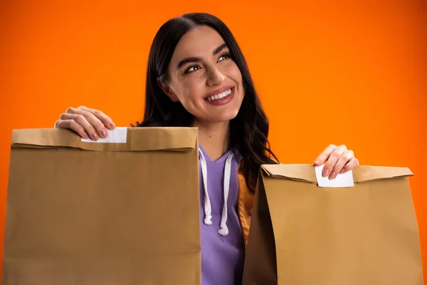 Dreamy young woman holding paper bags isolated on orange - foto de stock