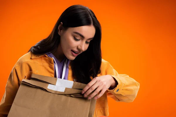 Jolie femme brune tenant des sacs en papier à emporter isolés sur orange — Photo de stock