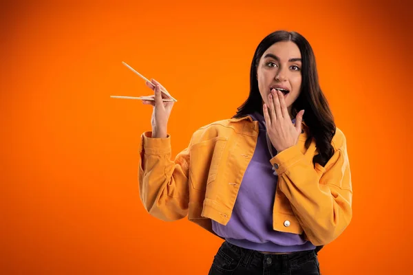 Excited woman holding chopsticks and looking at camera isolated on orange — Stockfoto