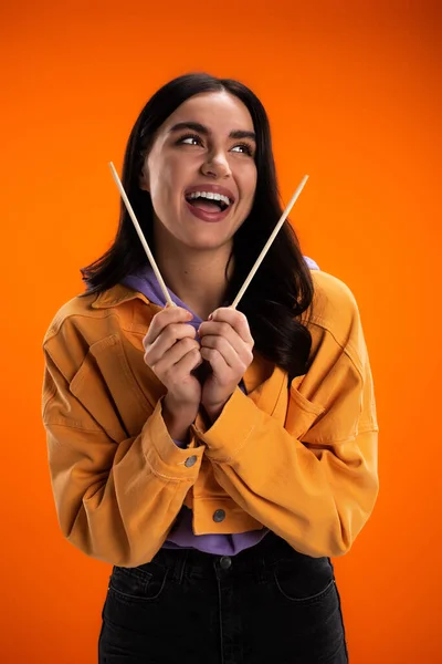 Fröhliche junge Frau hält Bambusstäbchen in der Hand und schaut vereinzelt auf Orange weg — Stockfoto