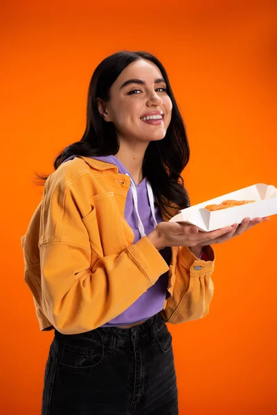 Positive woman holding takeaway sushi and smiling at camera isolated on orange — Stockfoto